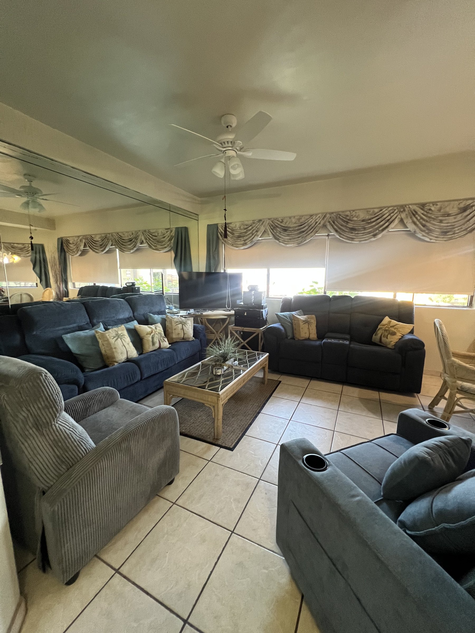 Wide view of the living room with two navy sofas, recliners, a glass-top coffee table and a mirrored wall