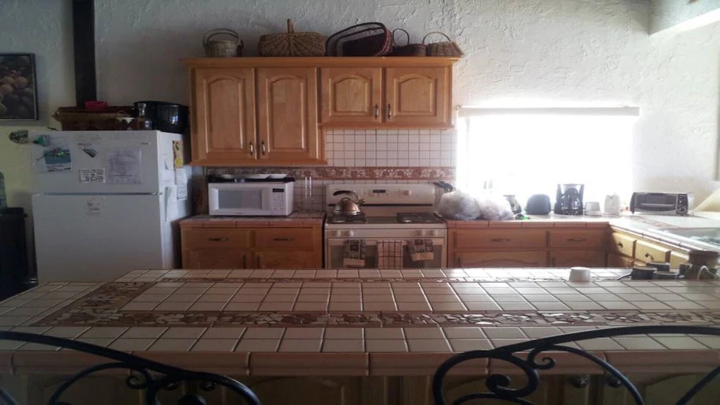 Kitchen with light wood cabinets, tiled counters, electric range, microwave and a long tiled breakfast bar