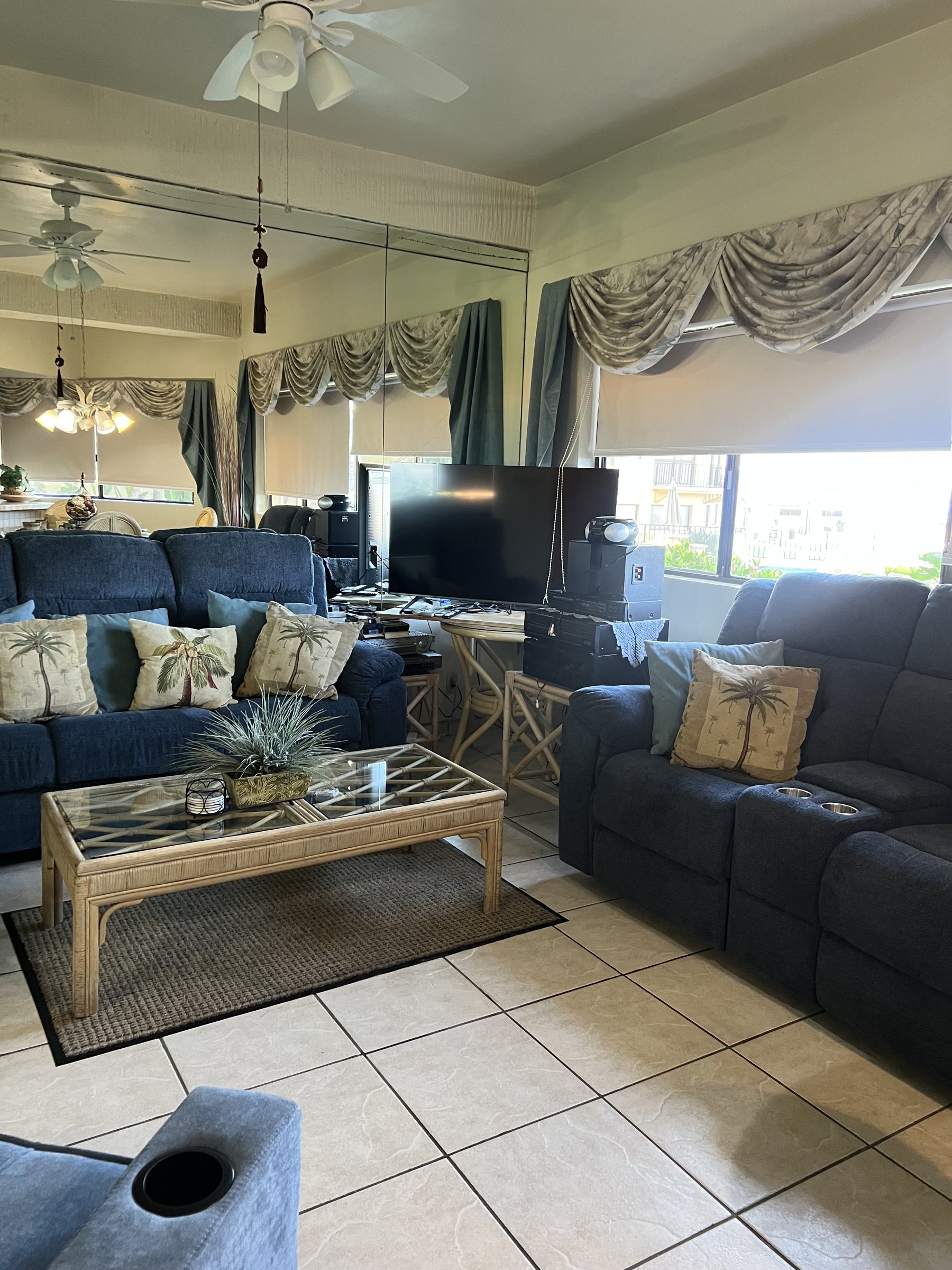 Navy sofas with palm-print cushions facing a flat-screen television, ceiling fan overhead