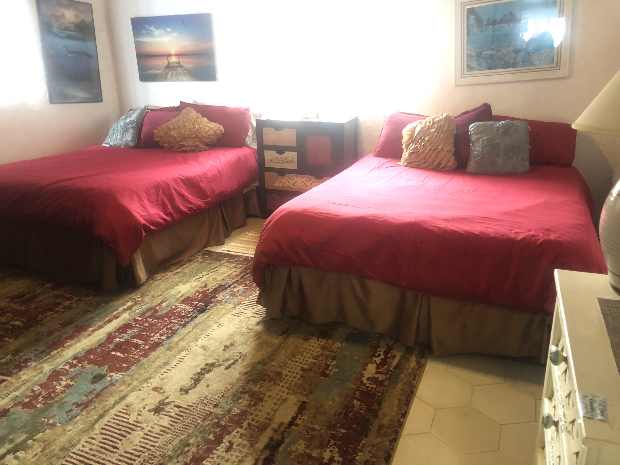 Bedroom with two beds in red bedding, a shared nightstand and coastal artwork on the walls