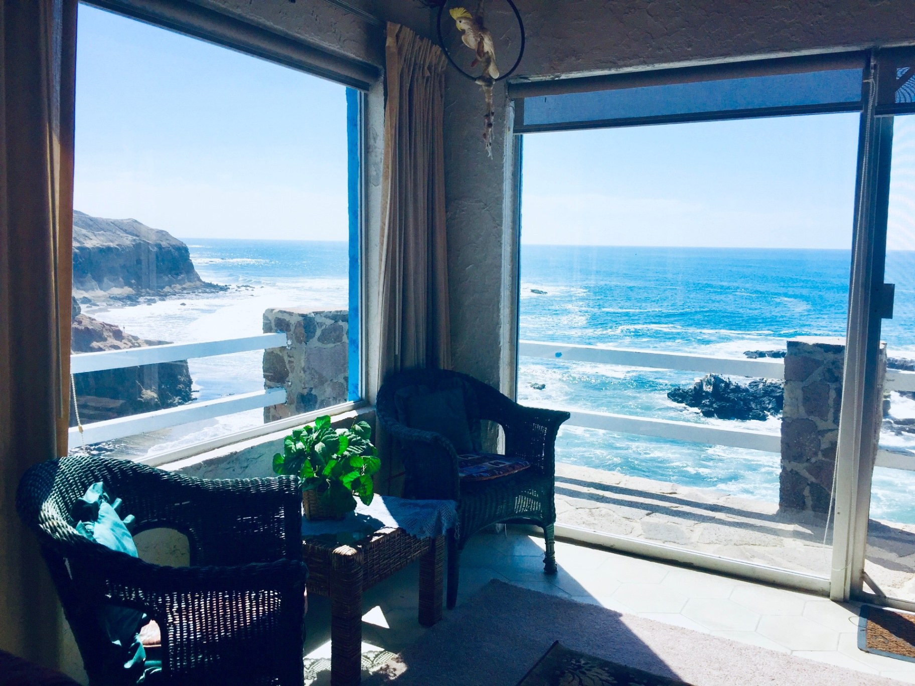 Corner sitting room with wicker chairs and floor-to-ceiling windows looking out to the ocean and cliffs