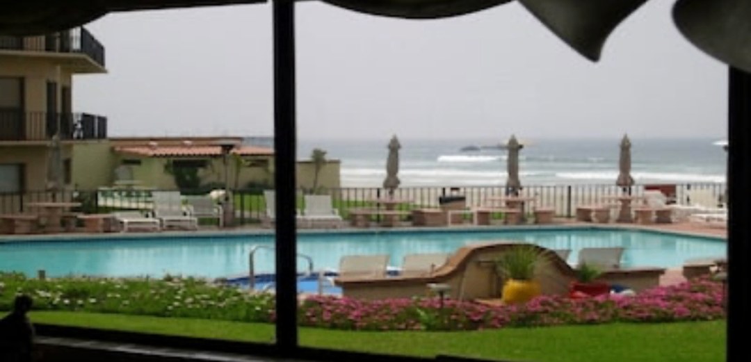 Pool, flower beds and breaking waves seen through a window from inside the condo