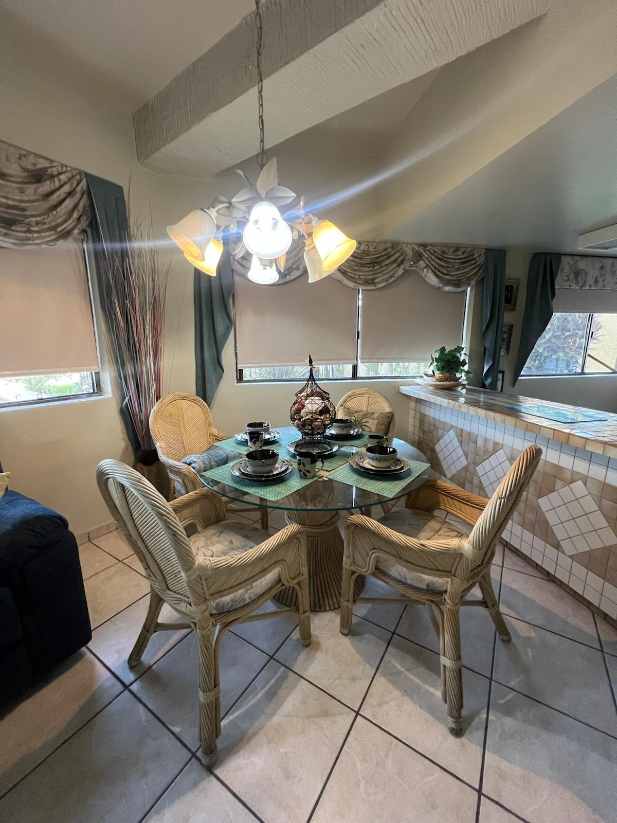 Rattan dining set for four with a glass table, place settings and a tiled breakfast bar behind