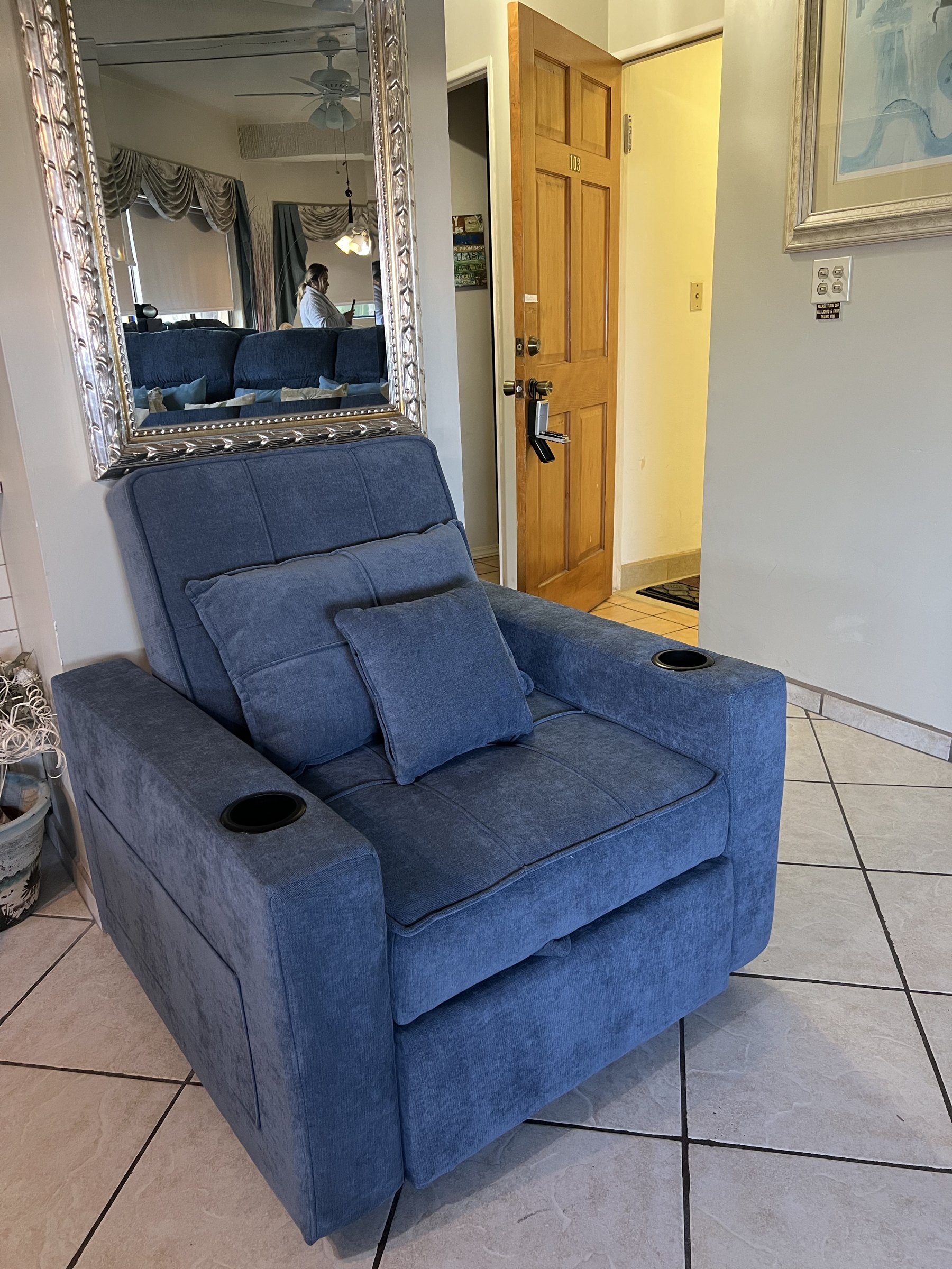 Blue upholstered recliner with cup holders beside a framed mirror near the entry hallway