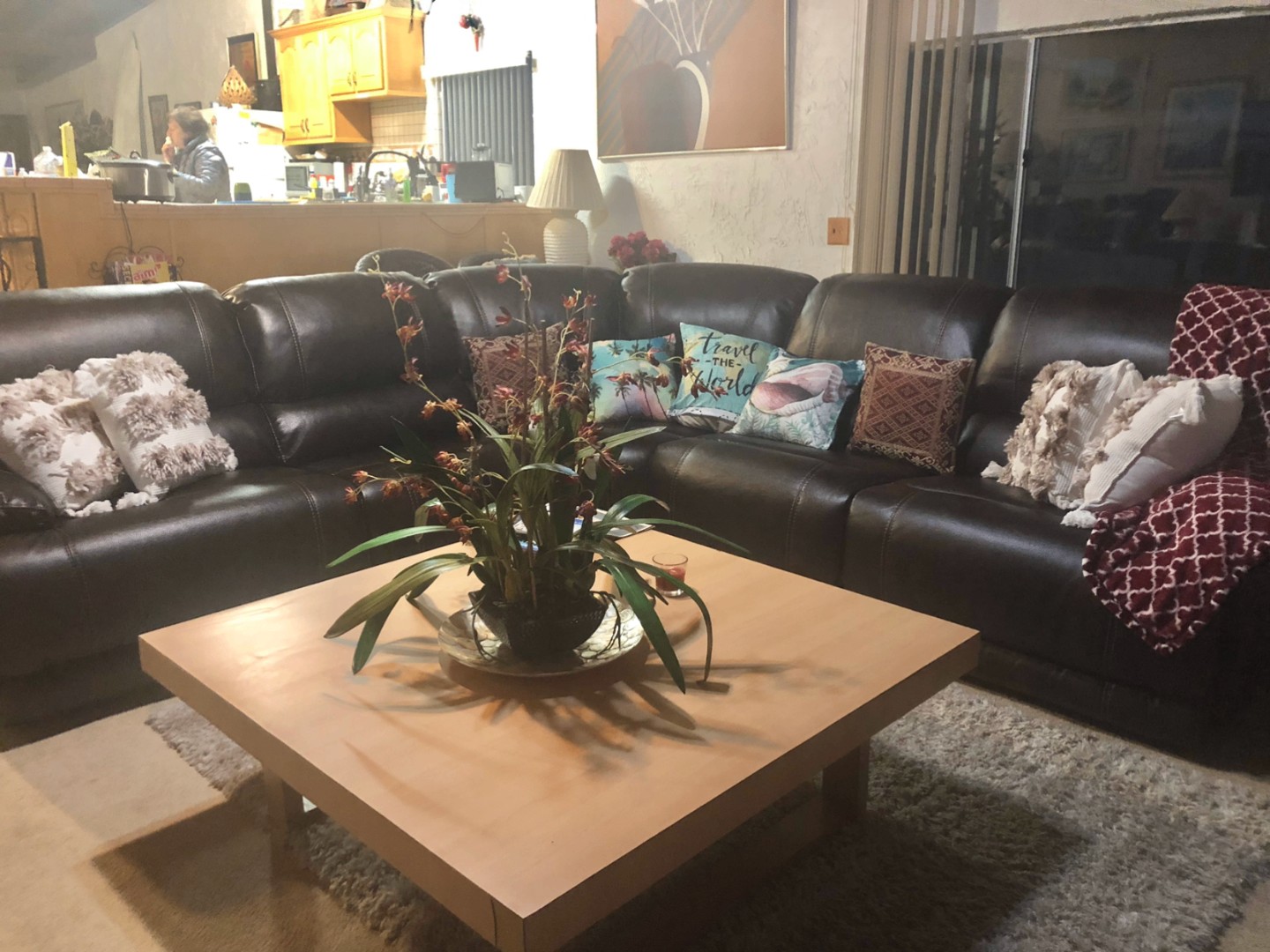 Living room with a large leather sectional, pillows and a low wood coffee table, open to the kitchen