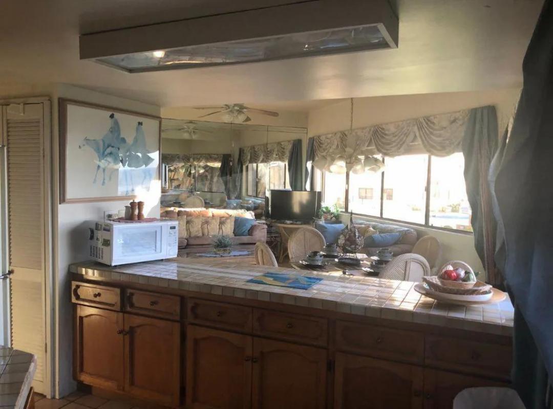 Tiled kitchen breakfast bar with wood cabinets and microwave, open to the living and dining area