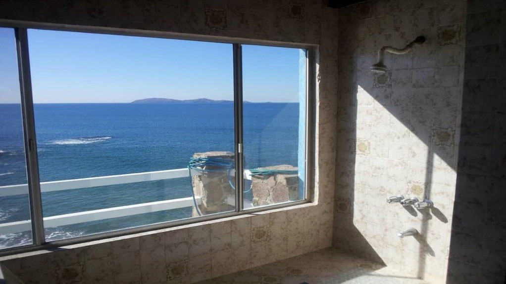 Tiled bathroom shower with a large window looking out to the ocean and distant islands