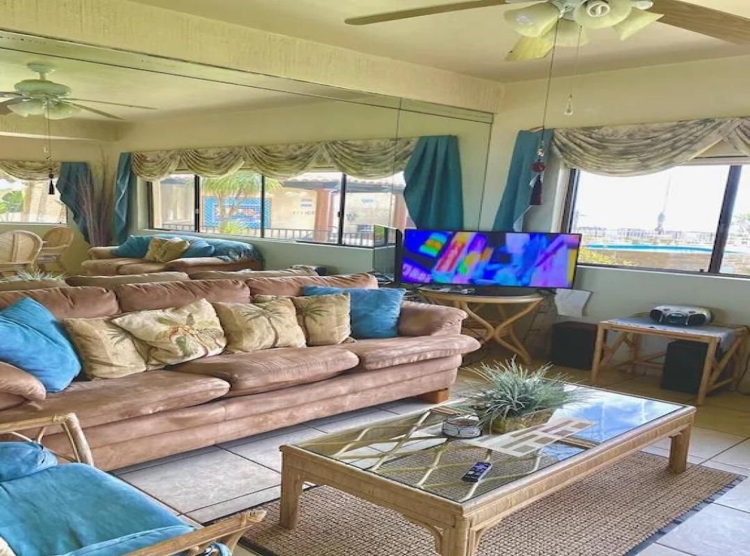 Living room with leather sofas, teal cushions, ceiling fans and windows looking out to the pool