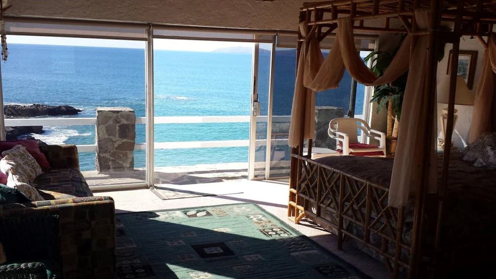 Master with a bamboo canopy bed and sliding glass doors opening to an oceanfront terrace over the surf