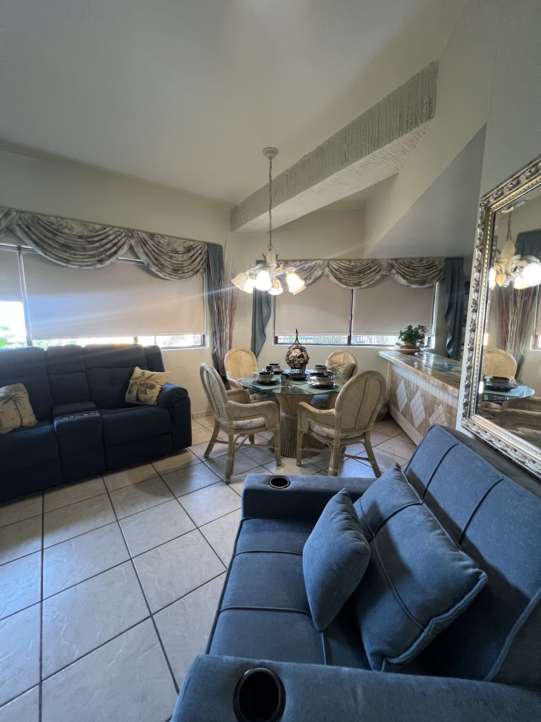 Open living and dining space with a glass-top rattan dining table set for four beneath a chandelier