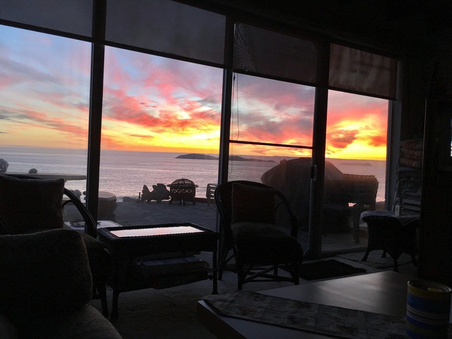 Sunset over the Pacific seen through the living room's sliding glass doors, with the patio fire pit outside