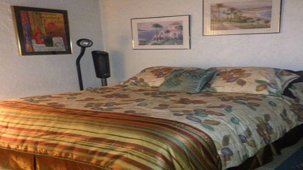 Flex room with a queen bed in floral bedding, reading lamp and framed coastal artwork