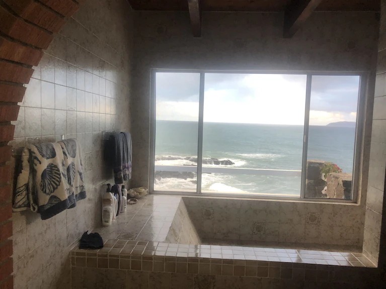 Tiled bathroom with a built-in tub and a large window overlooking the Pacific surf and rocky coastline