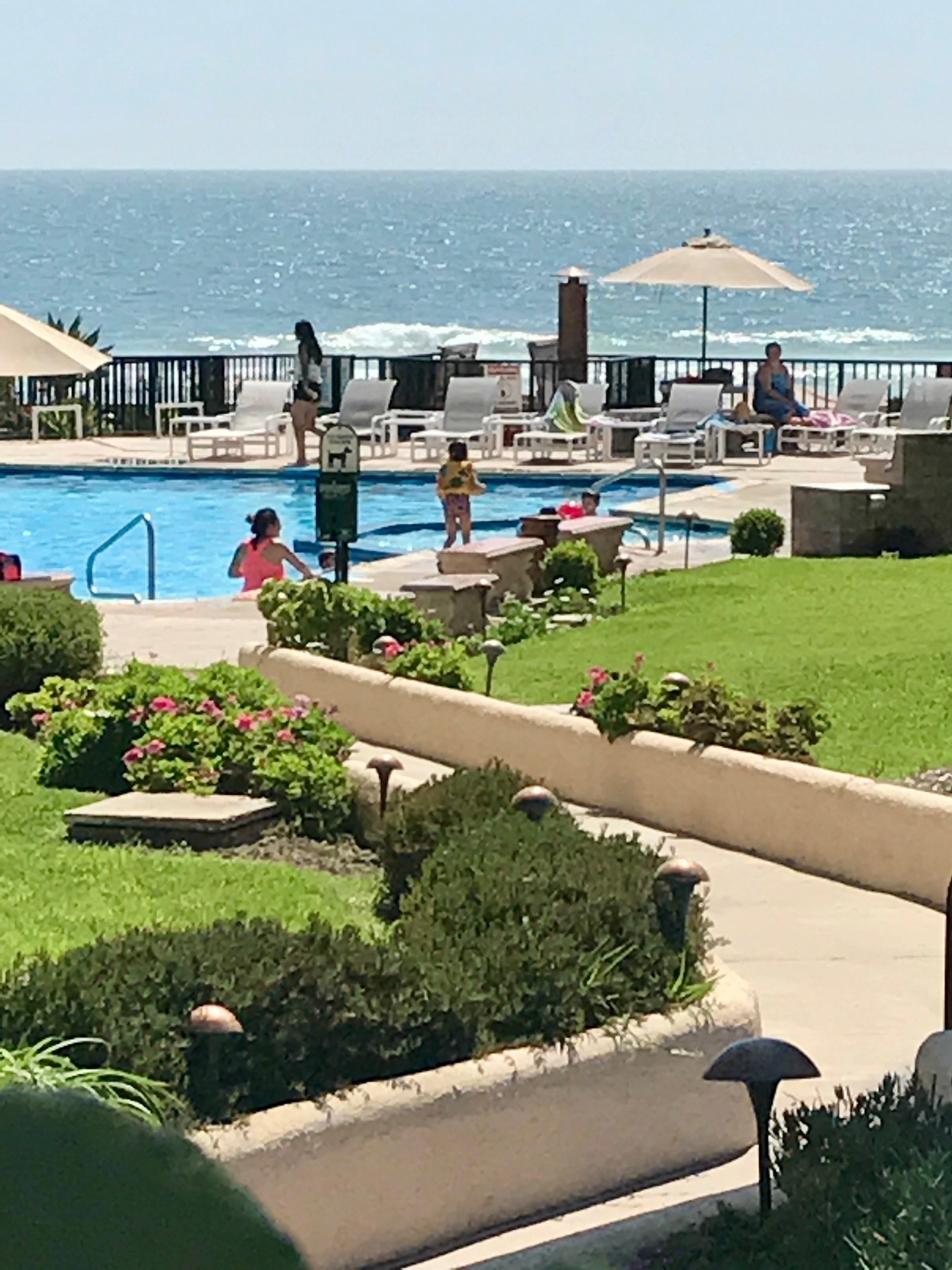 Swimming pool with lounge chairs and umbrellas on the deck, the Pacific surf directly beyond