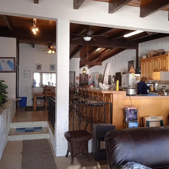 Open interior with exposed wood-beam ceilings, leather sofa, kitchen bar and dining area beyond